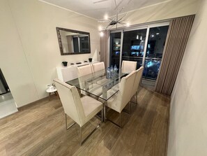 A modern dining area with a glass table and white chairs, a large mirror, and a view of the city at night.