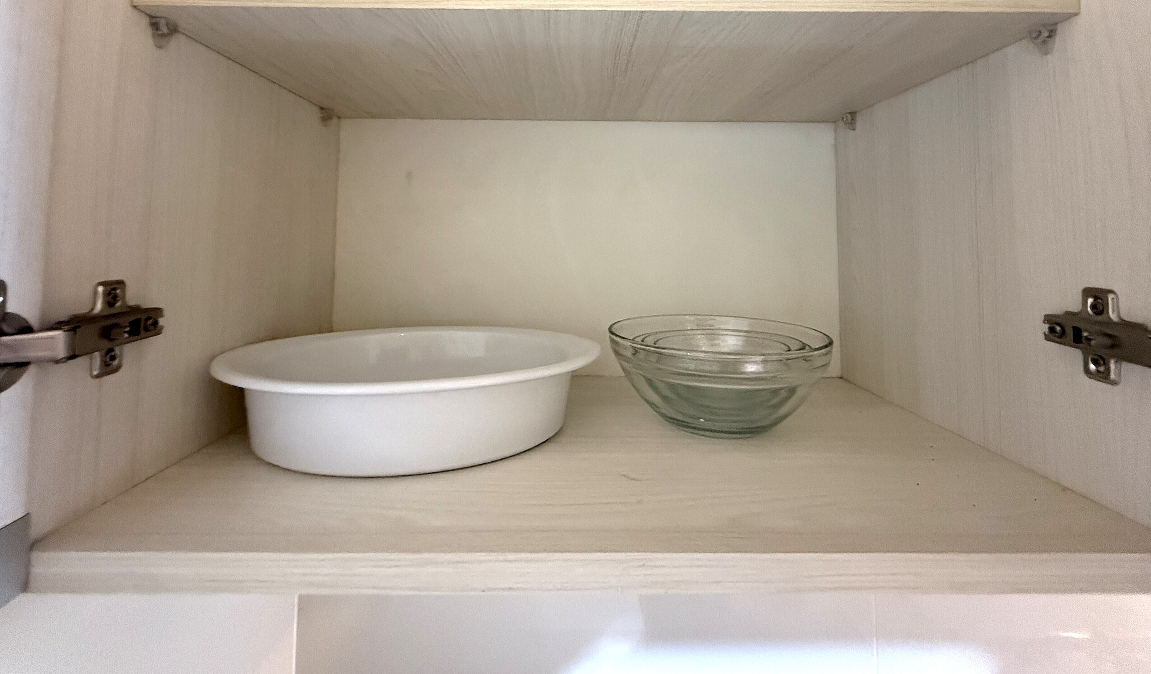 A small, empty cabinet with a white bowl and a clear glass bowl inside.