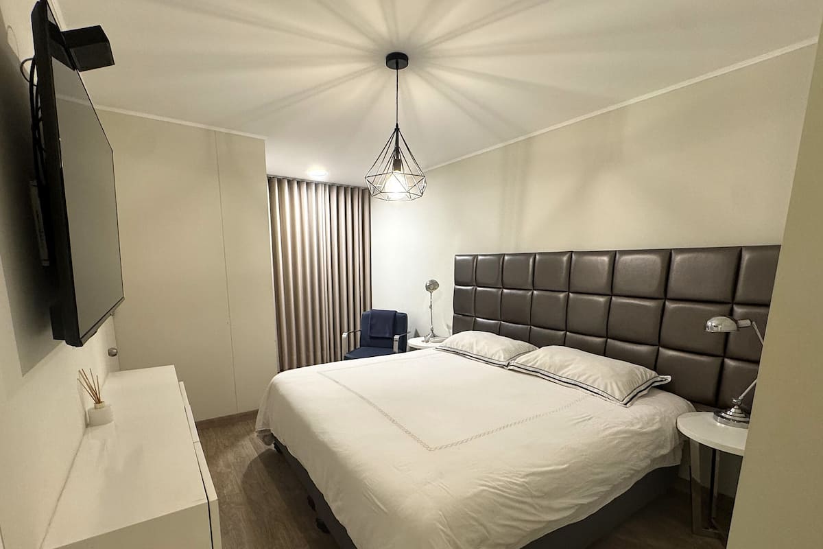 Une chambre d’hôtel comprenant un grand lit, une table de chevet, une chaise, un bureau, un téléviseur à écran plat et un luminaire au plafond.