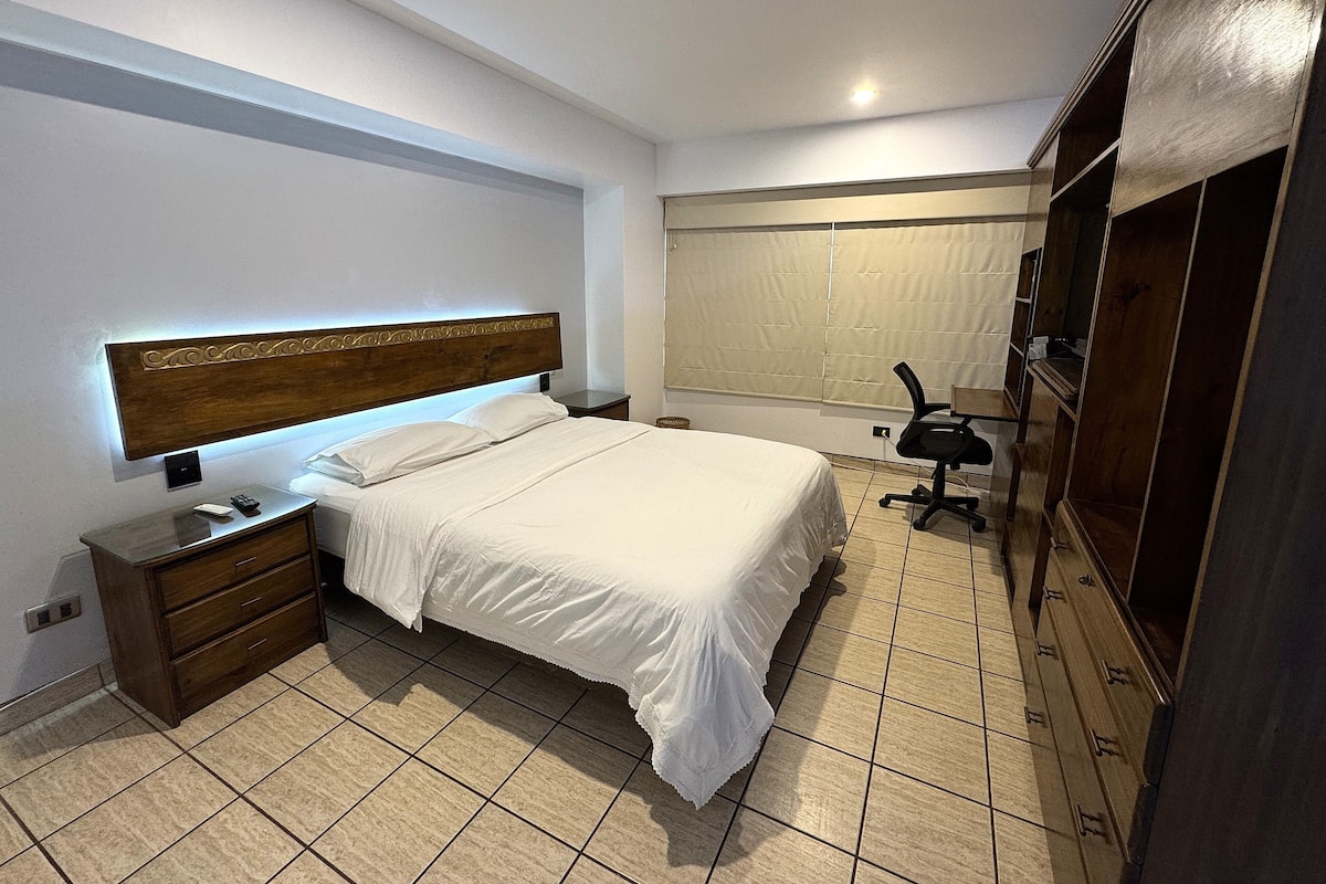 Une chambre bien rangée, avec un lit, une table de chevet et un bureau avec une chaise.