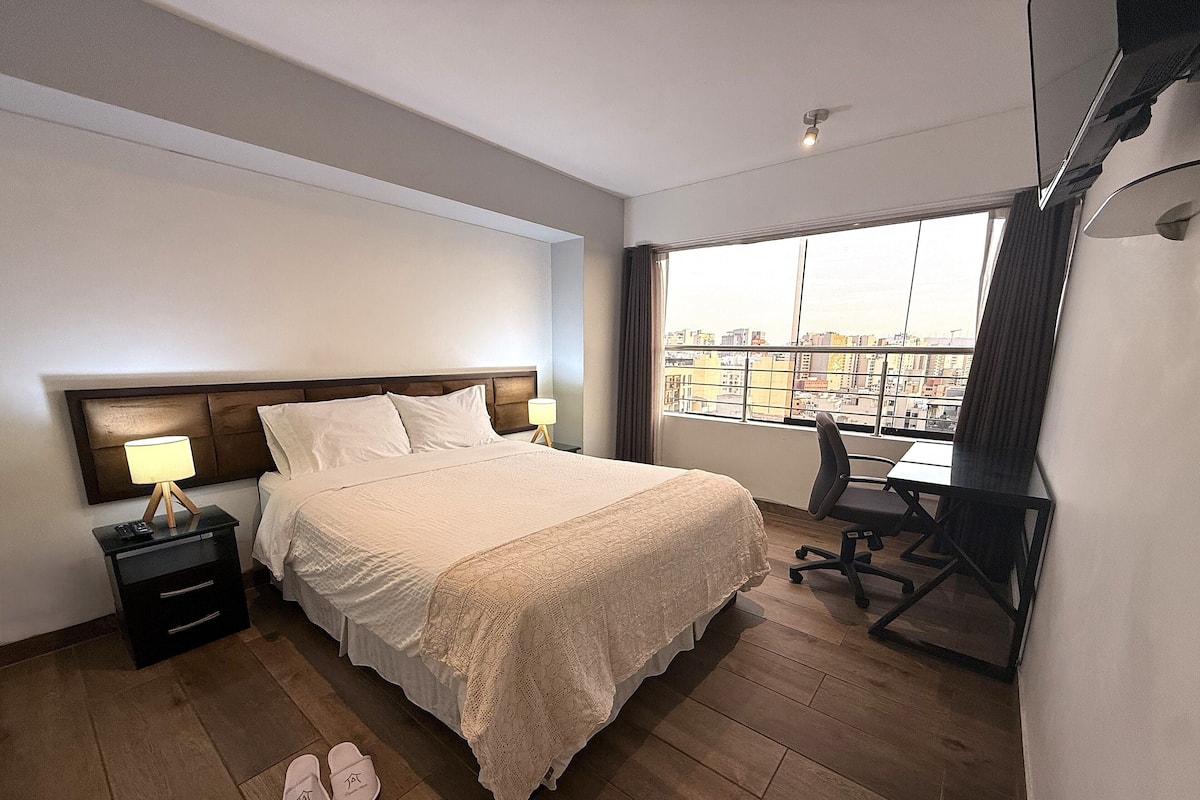 Une chambre d’hôtel avec un lit, une table de chevet, un bureau et une grande fenêtre.