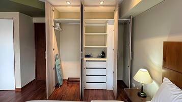 Une chambre d’hôtel comprenant un lit, une table de chevet avec une lampe, une armoire avec un miroir et une porte donnant sur une autre pièce.