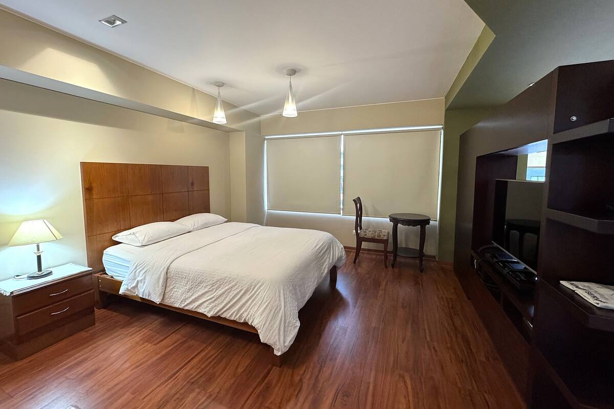 Une chambre à coucher avec un lit en bois, une table de chevet, une lampe, une chaise, une petite table et un téléviseur.