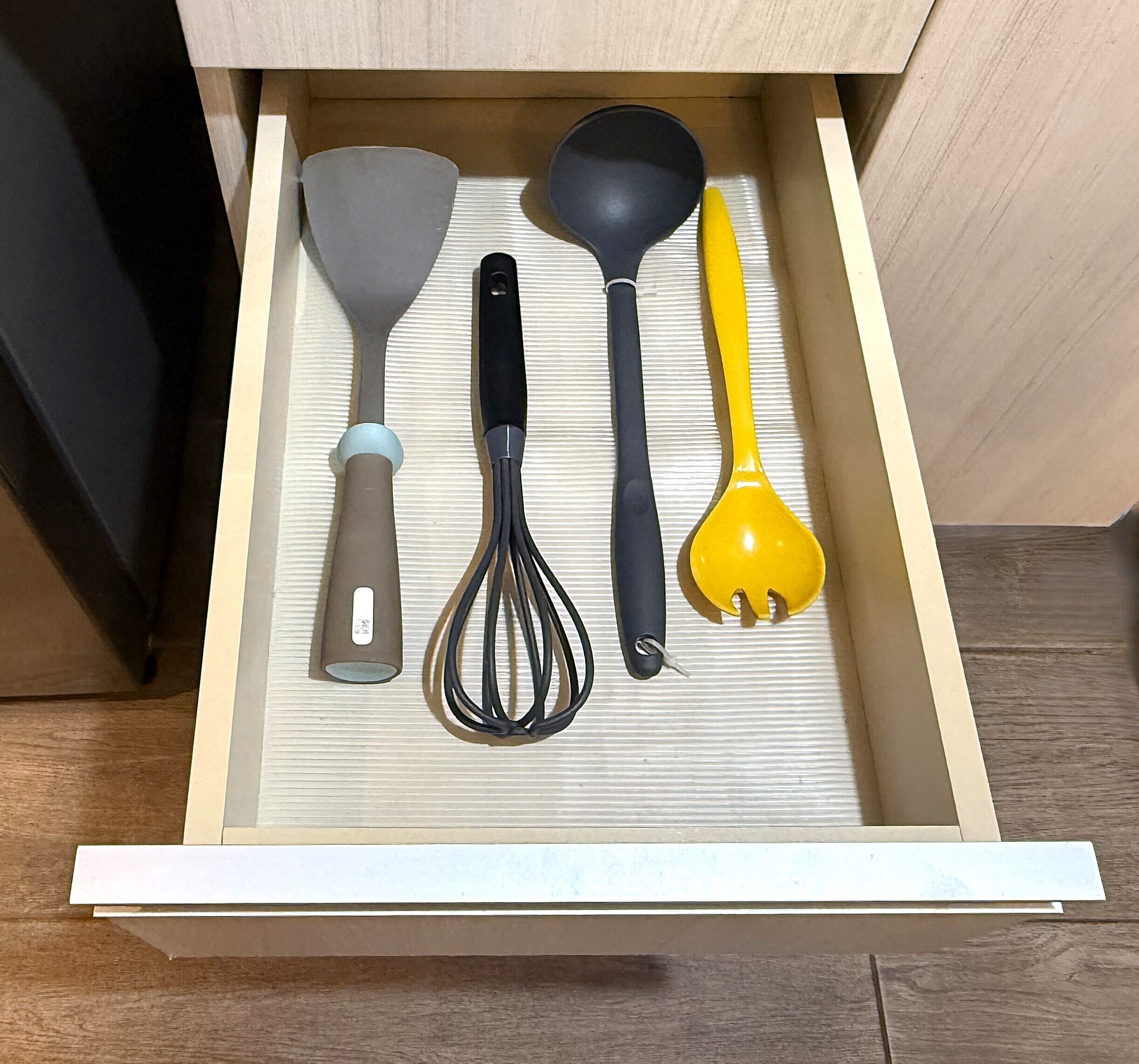 A drawer with kitchen utensils including a spatula, whisk, and ladle.