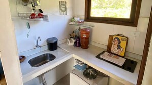 Una cocina compacta con un lavamanos, un refrigerador pequeño, una ventana y una estantería con utensilios de cocina.