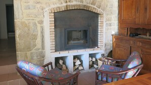 Una chimenea de piedra con un inserto moderno, sillas de madera con cojines de colores y un aparador de madera a la derecha.