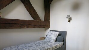Una habitación pequeña con cama individual, techo de madera, mesita de noche y lámpara de pared.