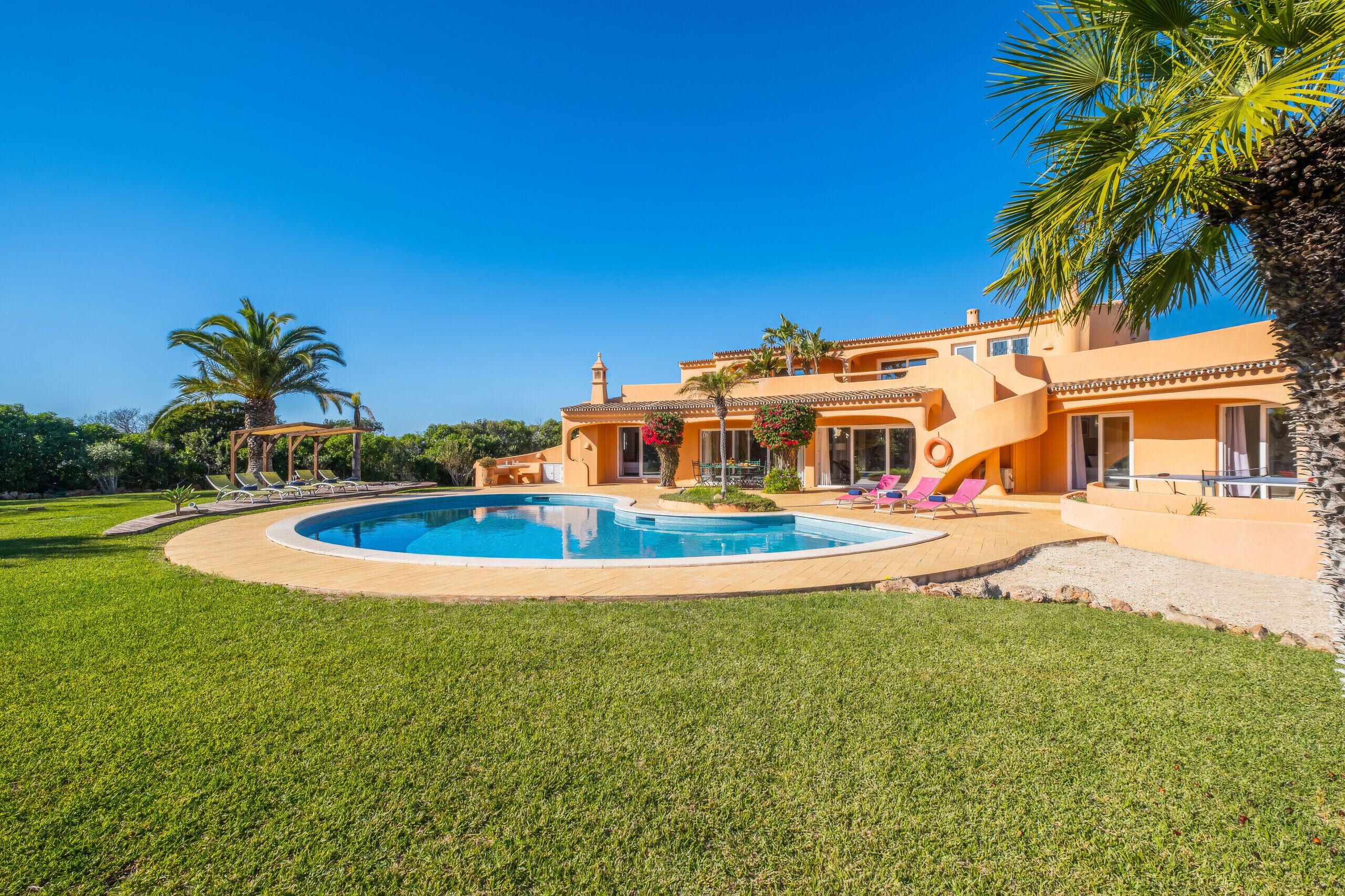 Una casa con piscina, palmeras y cielo azul despejado.