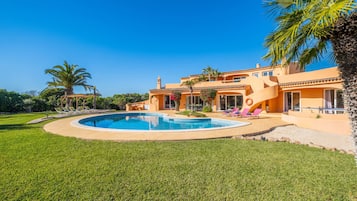 Una casa con piscina, palmeras y cielo azul despejado.