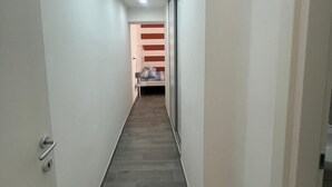 Kapea käytävä, jonka perällä näkyy sänky, vasemmalla puolella ovi ja katossa valaisin.