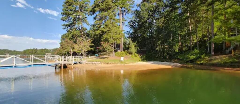 Un cadre paisible au bord d’un lac, avec une jetée en bois s’avançant dans l’eau, entouré d’arbres denses et sous un ciel dégagé.
