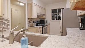 A kitchen with a marble countertop, stainless steel appliances, and beige cabinetry.