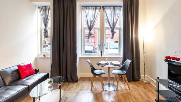 Una sala de estar moderna con un sofá, una mesa de centro de vidrio, una mesa de comedor con sillas y un televisor.