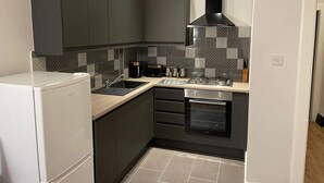 Una cocina compacta con armarios oscuros, un refrigerador blanco, salpicadero de azulejos y horno empotrado.