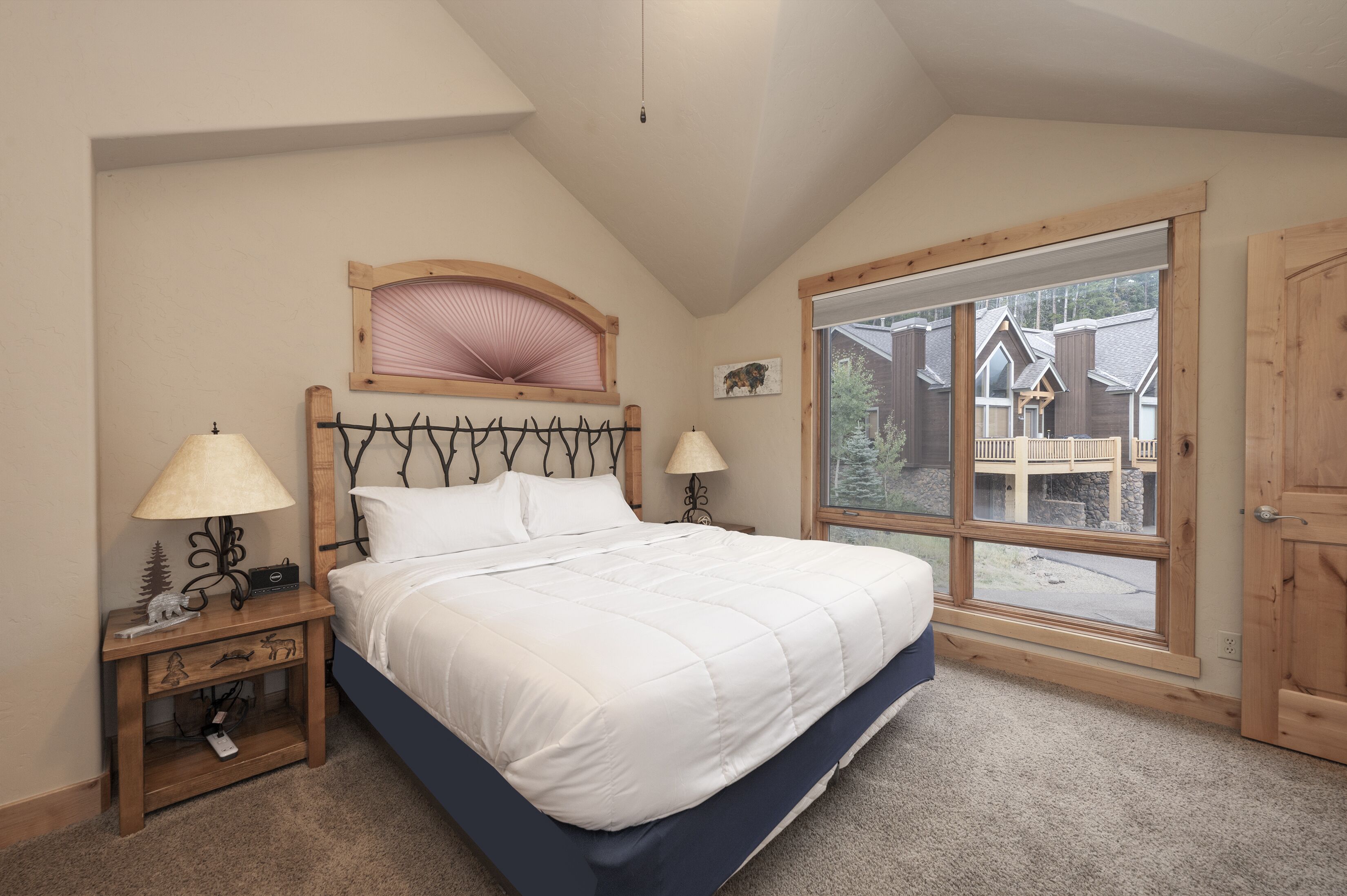 A bedroom with a large bed, two bedside tables with lamps, a window with a view of a building, and a wooden headboard.
