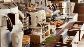 A buffet setup with a coffee machine, various food items, and a stone wall background. - Villa Kapresse du 978 (Marigot)