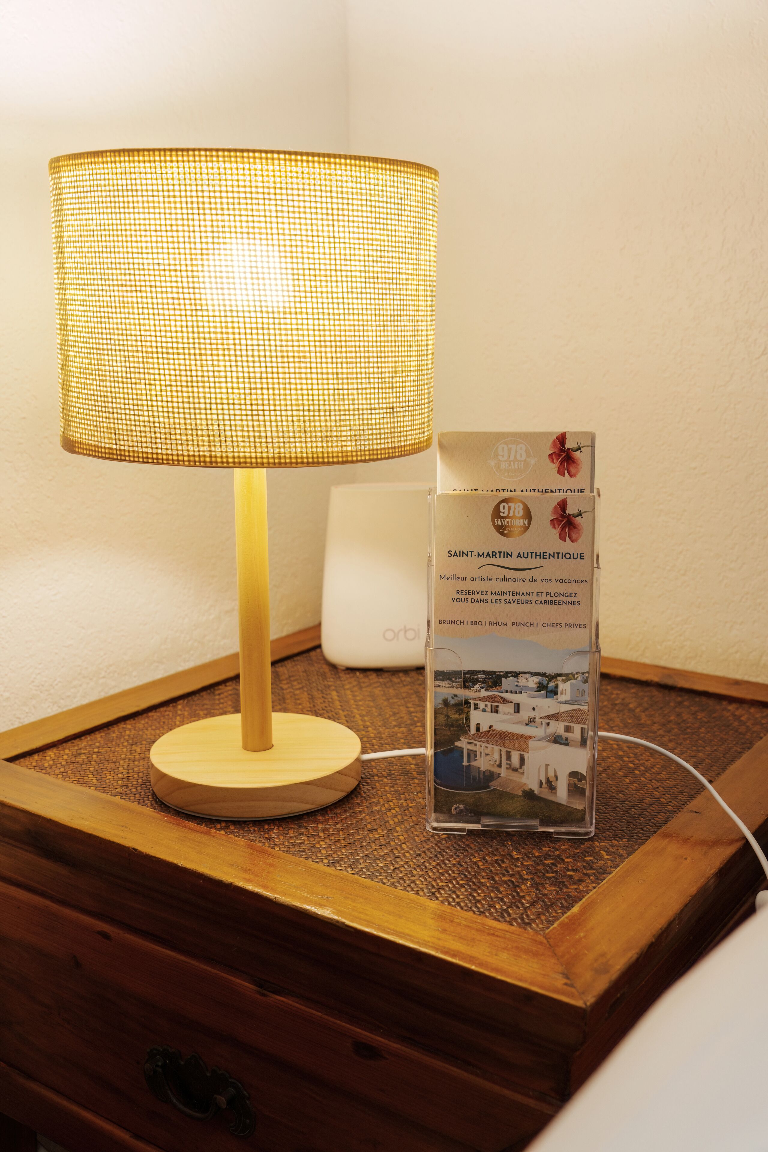A bedside table with a lamp, a brochure, and a white device on a textured surface.
