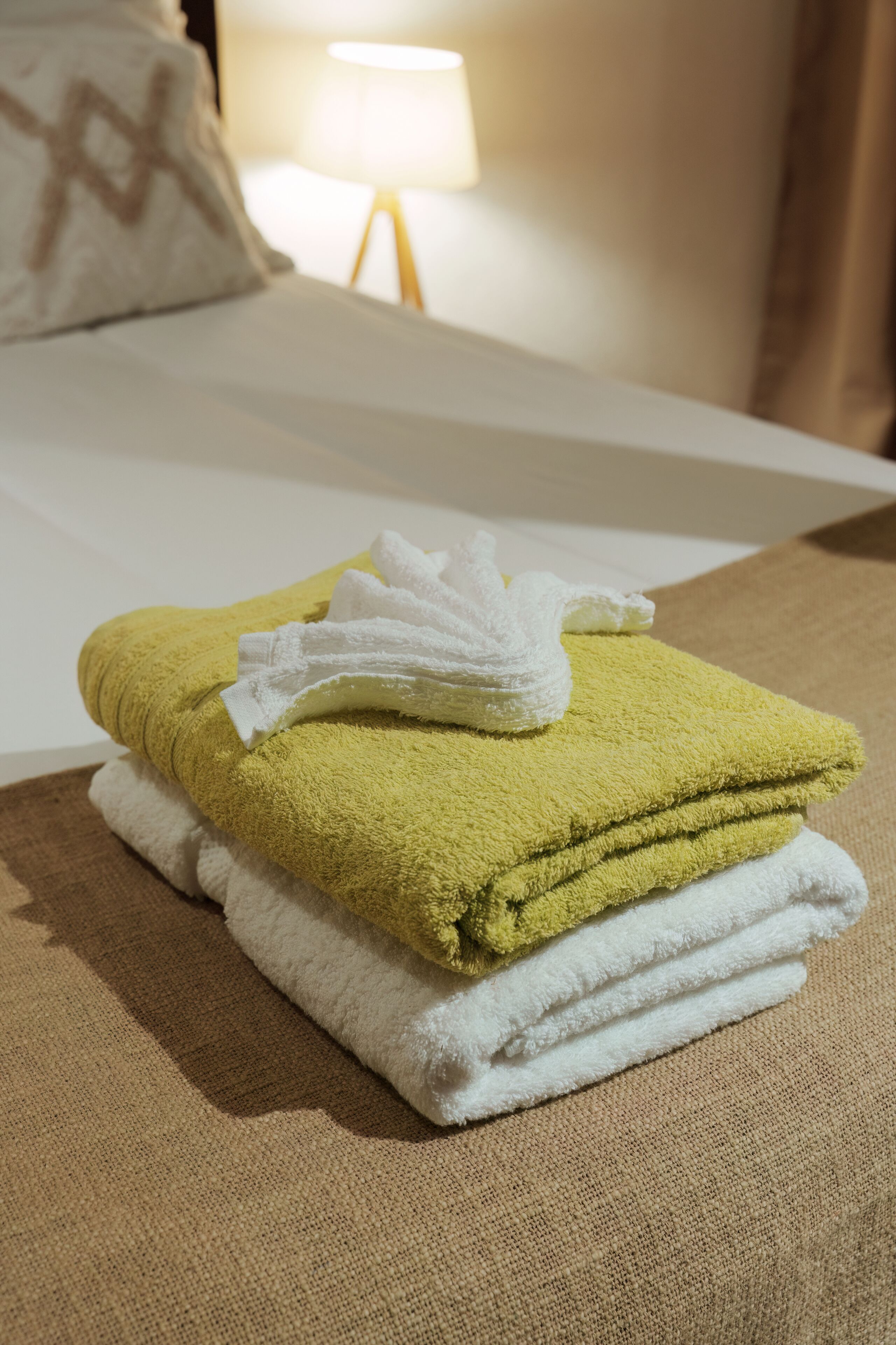 Un lit bien fait, avec une couette blanche et une serviette jaune pliée posée sur le dessus.