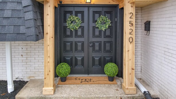 A black double door with two wreaths, a wooden porch, and a mailbox.