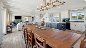 A spacious kitchen with a wooden dining table, blue cabinets, and a large window offering a view of the outdoors.