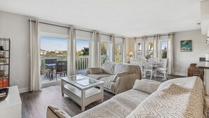 A spacious living room with a large glass table, a sofa, and a dining area with chairs. - Heated Pool! 3min walk to the beach! Gorgeous Intercoastal Views!  (Indian Shores)
