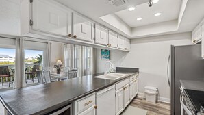 A modern kitchen with white cabinets, a stainless steel refrigerator, and a large window overlooking a balcony. - Heated Pool! 3min walk to the beach! Gorgeous Intercoastal Views!  (Indian Shores)