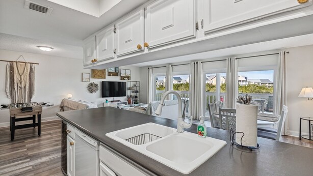 A modern kitchen with white cabinetry, a double sink, and a large window overlooking a balcony. - Heated Pool! 3min walk to the beach! Gorgeous Intercoastal Views!  (Indian Shores)