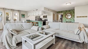 A modern living room with a sofa, a glass coffee table, and a kitchen area in the background. - Heated Pool! 3min walk to the beach! Gorgeous Intercoastal Views!  (Indian Shores)