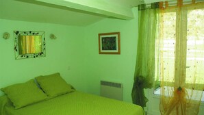 A room with a bed, a radiator, a window with sheer curtains, and two framed pictures on the wall.