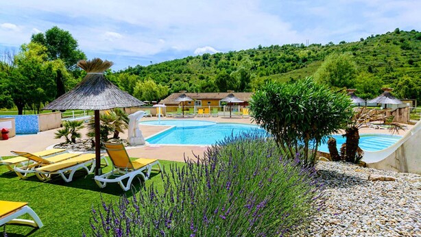 A pool area with lounge chairs, a thatched umbrella, and a view of a hillside.