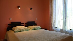 Une chambre à coucher avec un lit, deux lampes fixées au mur et des rideaux légers.