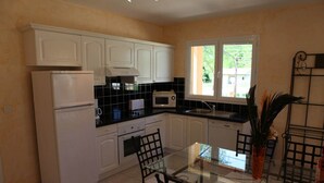 Une cuisine de taille réduite, avec des meubles blancs, un réfrigérateur, un four à micro-ondes et une table à manger avec des chaises.