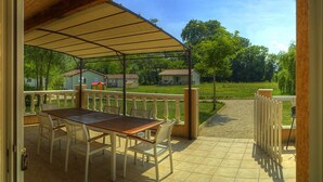 Une terrasse extérieure avec une table et des chaises couvertes, une vue sur des maisons en arrière-plan et un espace délimité par une clôture.