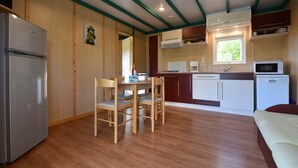 A compact kitchen with wooden cabinets, a refrigerator, a microwave, and a dining table with chairs. - Chalet 3 people (MONTREAL)