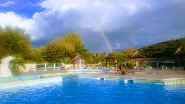 A swimming pool with lounge chairs and umbrellas, surrounded by trees and a hill. - Chalet 3 people (MONTREAL)