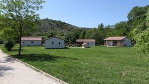 A rural setting with three white buildings with red roofs, surrounded by green grass and trees, with a hill in the background. - Chalet 3 people (MONTREAL)