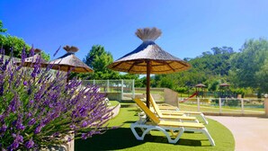 A garden with thatched umbrellas, a pool area, and a playground. - Chalet 3 people (MONTREAL)