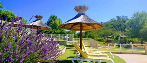 A garden with thatched umbrellas, a pool area, and a playground.