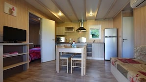 A compact living space with a kitchenette, a dining area with two chairs, a television, and a bed with a floral bedspread. - Chalet 5 people (MONTREAL)
