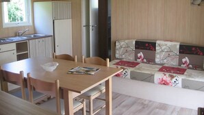 A compact kitchen with a sink, cabinets, and a dining table with chairs. There is a sofa with floral cushions and a small window. - Chalet 5 people (MONTREAL)