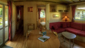 Une pièce chaleureuse avec une table à manger en bois, un canapé et une petite table. On y trouve une fenêtre avec des rideaux, une porte et un radiateur.