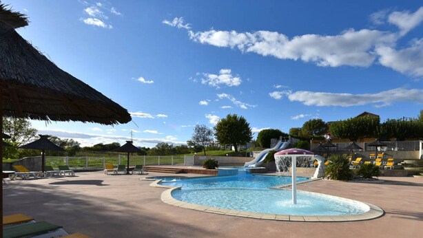 A swimming pool with a water slide, lounge chairs, and a thatched roof structure.