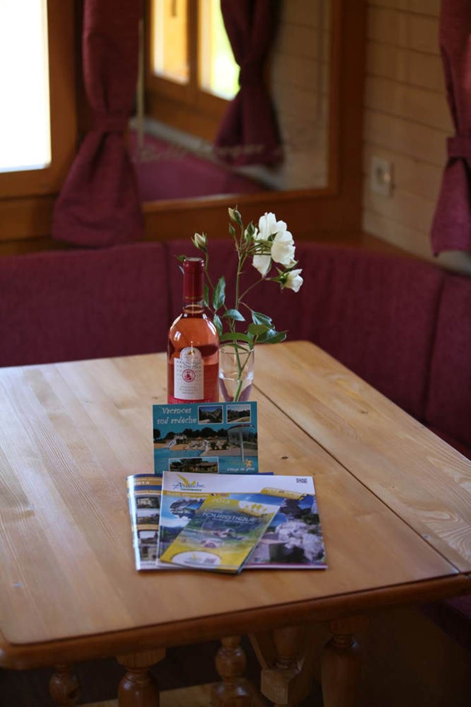 A wooden table with a bottle, a vase with white flowers, and a brochure.