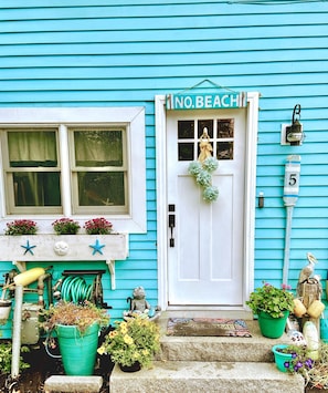 Una casa turquesa con una puerta blanca que indica 'NO. BEACH' y un cartel con el número 5.