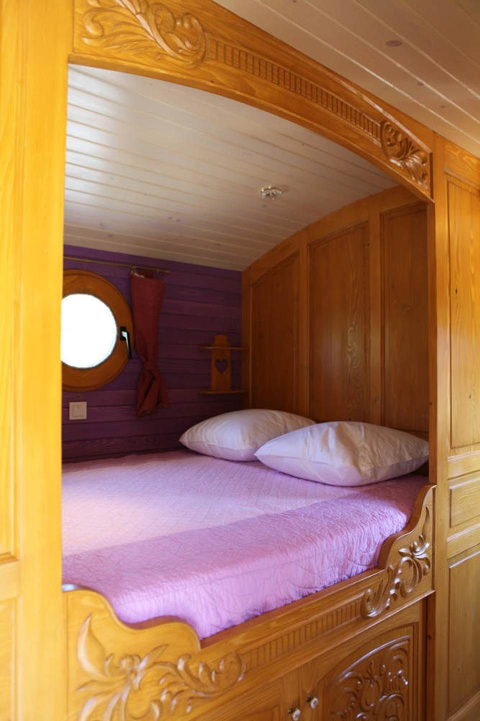 Una cama litera de madera con un ventanal circular, una pared morada y un cabecero de madera.