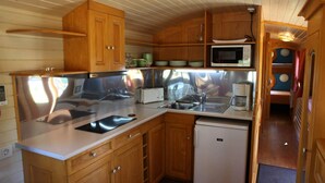 A compact kitchen with wooden cabinets, a microwave, a sink, and a small refrigerator. - 4/5 people trailers (MONTREAL)