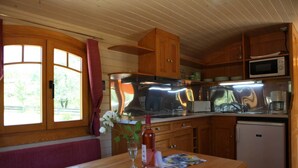 A compact kitchen with wooden cabinets, a microwave, a refrigerator, and a dining area with a table and bench. - 4/5 people trailers (MONTREAL)