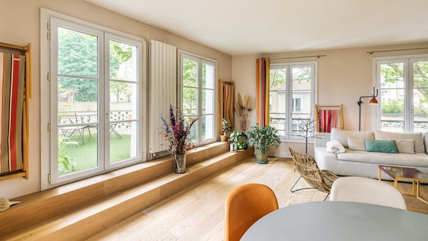 Un salon lumineux avec de grandes fenêtres, un canapé, une table à manger et une chaise.