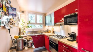 Une cuisine de taille réduite avec des meubles de couleur rouge, une cuisinière à gaz, un four à micro-ondes et un évier.