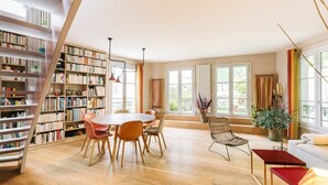 Une pièce spacieuse avec un grand escalier en bois, une table de salle à manger ronde entourée de chaises et une bibliothèque remplie de livres.